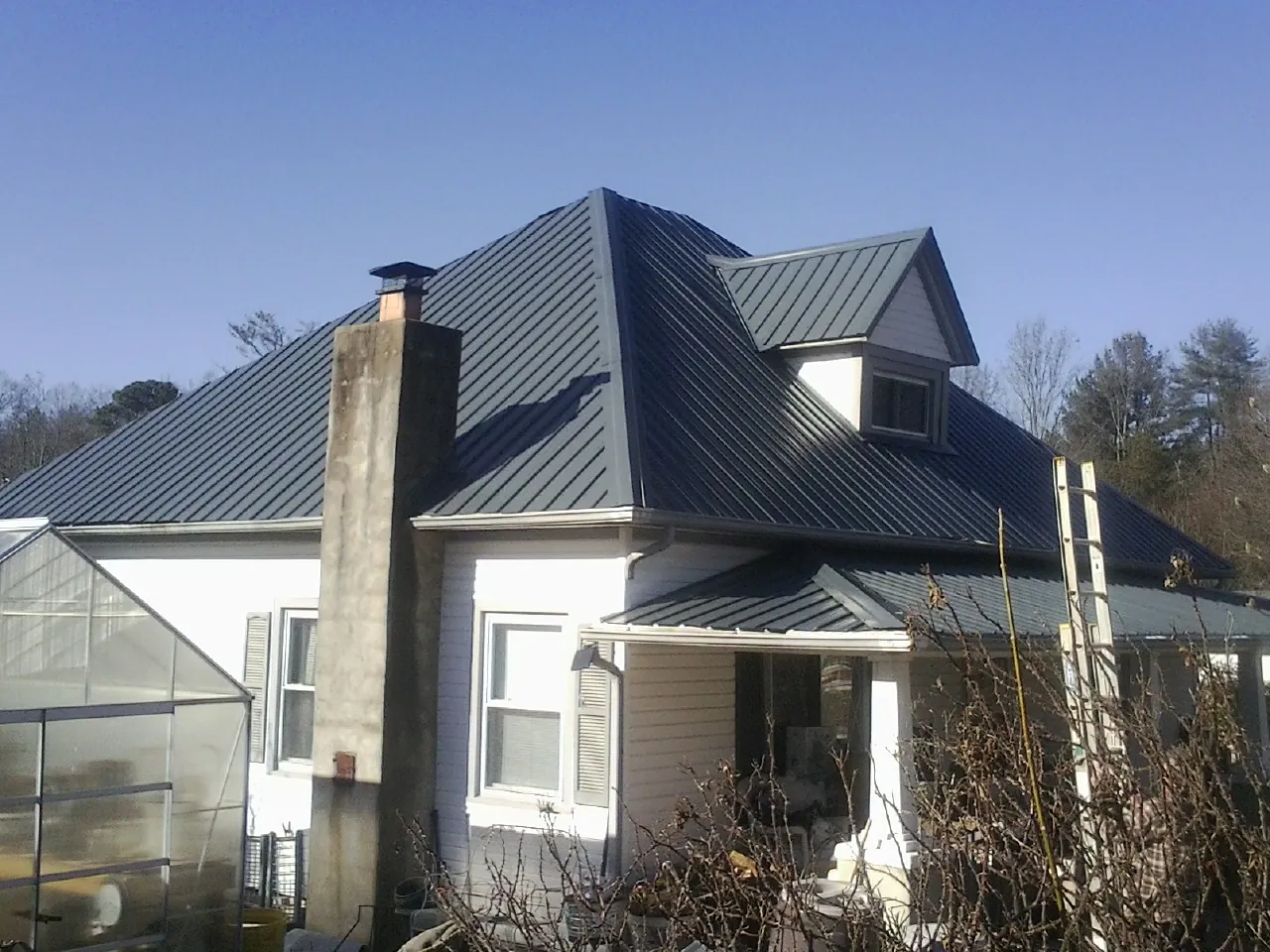 Dark blue standing seam metal roof on a white farmhouse with dormer — Slate & Tile Roof Repair by Roofing Brothers in Glendale