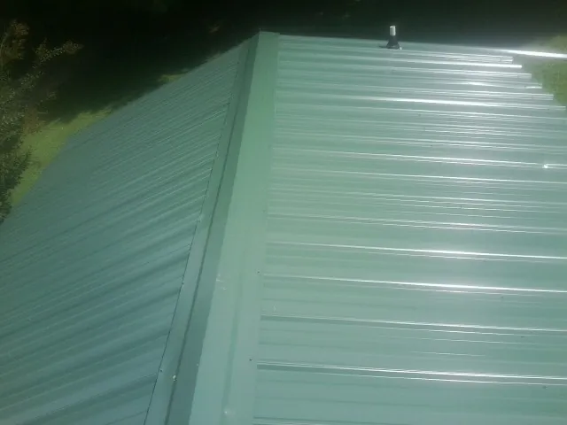 New green metal panels meeting at the ridge of a roof — Flat Roof Repair work by our crew in Glendale